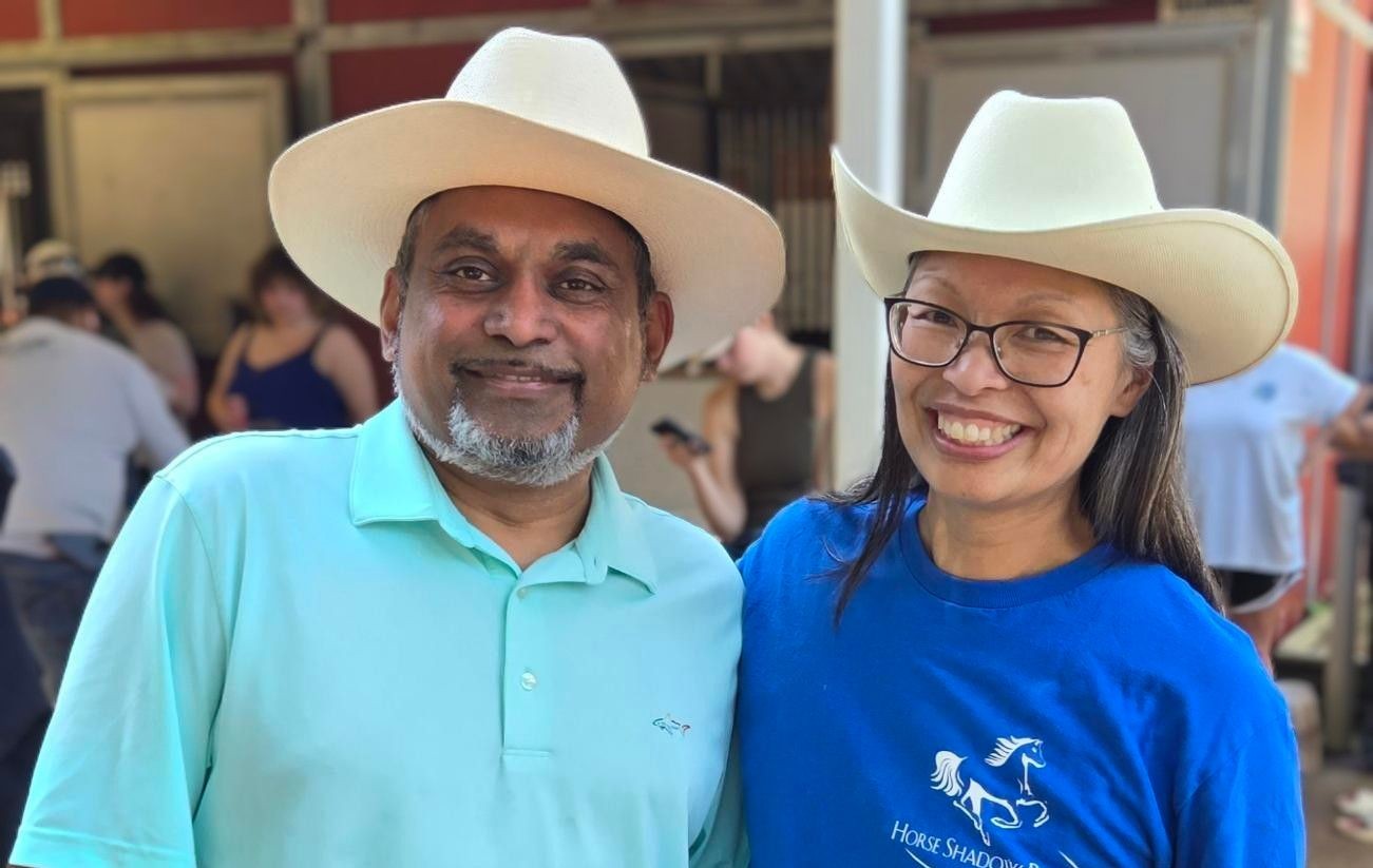 Two people wearing cowboy hats smiling, with a crowd in the background.